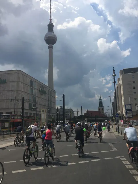 Ein Pulk Radfahrender auf einer breiten Straße, im Hintergrund der Fernsehturm