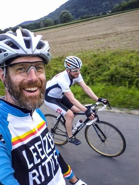 Selfie eines Fahrers mit Helm, dahinter ein Mitfahrer auf einer Landstraße
