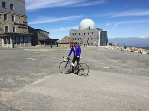 Ein Fahrer steht mit seinem Rad vor einem Berggasthaus mit Radarkuppel