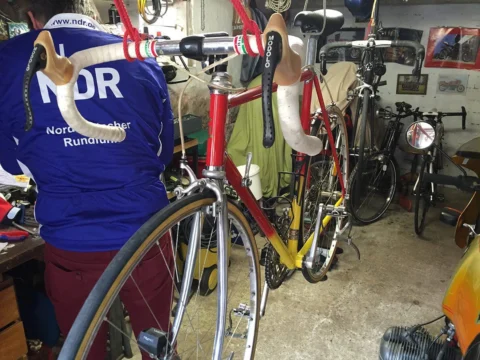 Ein rotes Rennrad in der Werkstatt, links jemand im NDR-Trikot