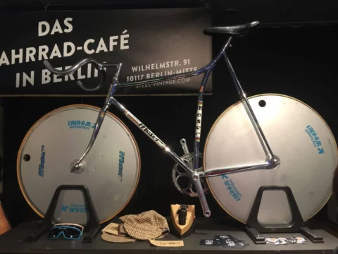 Ein Zeitfahrrad mit zwei Scheibenrädern in einer Vitrine, daneben Brille und Rennmütze