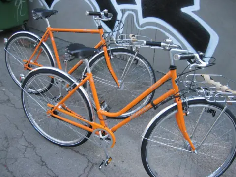 Ein orangefarbenes Damenrad im klassischen Stil an einer Graffitiwand