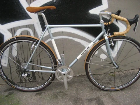 Ein silbernes Rennrad mit braunem Lenkerband an einer Graffitiwand
