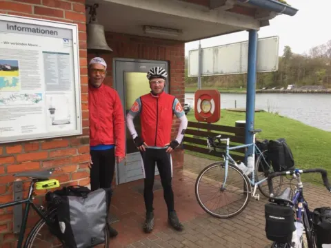 Zwei Radfahrer stehen mit ihren bepackten Rädern an einer Anlegestelle