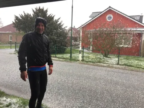 Ein Radfahrer auf einer schneebedeckten Dorfstraße vor einem roten Backsteinhaus