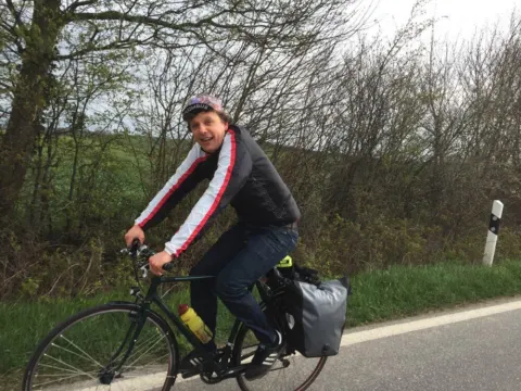 Ein Fahrer in schwarz-weißer Jacke auf einem bepackten Rad am Straßenrand
