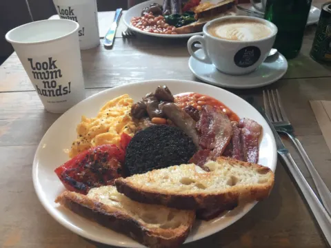Ein englisches Frühstück mit Bohnen, Speck und Toast, daneben Kaffee