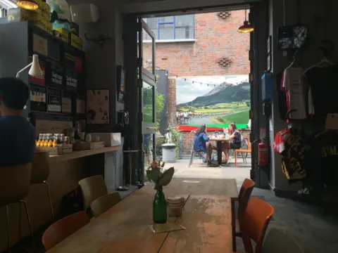 Blick durch ein Radcafé zur offenen Tür, an den Wänden Regale mit Waren