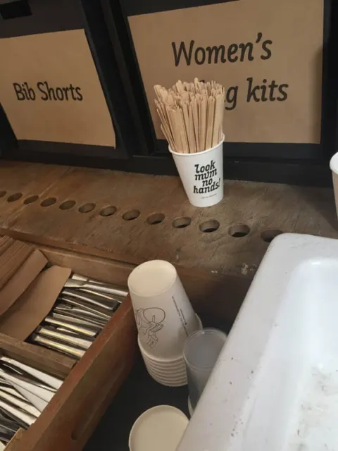 Ein Regal mit der Aufschrift „Women's Bib Shorts“, davor ein Becher mit Rührstäbchen