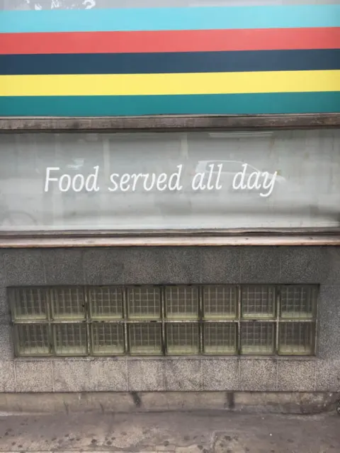 Eine Hauswand mit Regenbogenstreifen und dem Schriftzug „Food served all day“