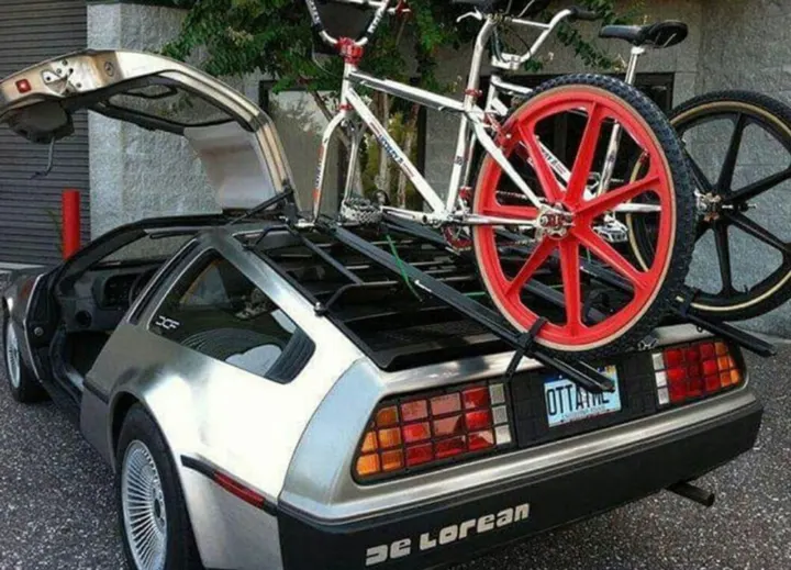 Zwei Rennräder auf dem Heckträger eines DeLorean, eines mit rotem Scheibenrad