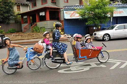 Eine Frau fährt mit mehreren Kindern auf Rädern und im Lastenrad eine Straße entlang