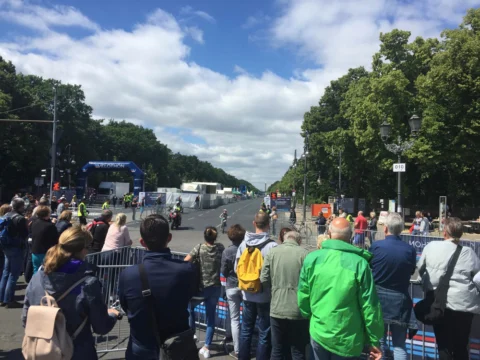 Zuschauer an der Absperrung einer breiten Allee, im Hintergrund der Zielbogen