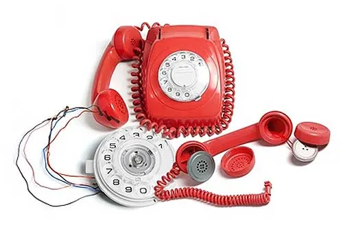 Ein rotes Wählscheibentelefon, daneben ein zweites in Einzelteile zerlegt