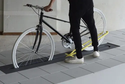 Ein Fahrrad rollt über eine schräge Platte im Boden, daneben steht ein Mensch