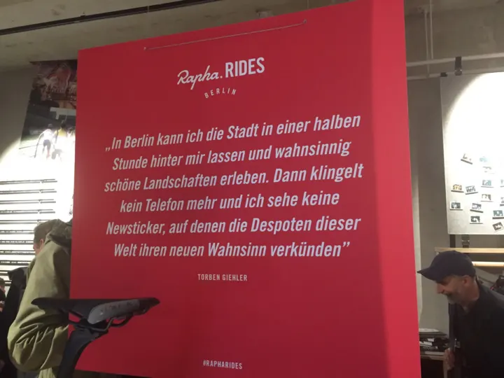 Eine rote Wandtafel mit einem Zitat über Ausfahrten in Berlin, davor Besucher