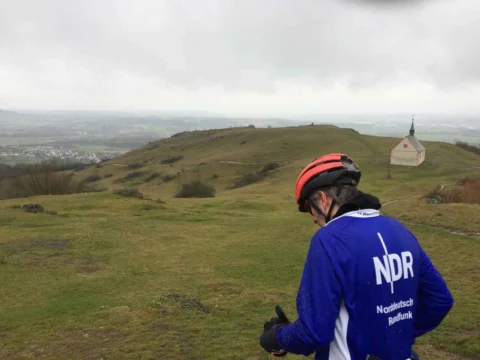 Ein Fahrer im blauen NDR-Trikot blickt über eine hügelige Landschaft