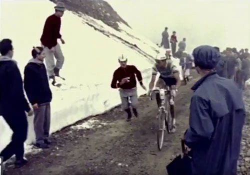 Historische Aufnahme: ein Fahrer kämpft sich eine schneebedeckte Rampe hinauf, daneben Zuschauer in Mänteln