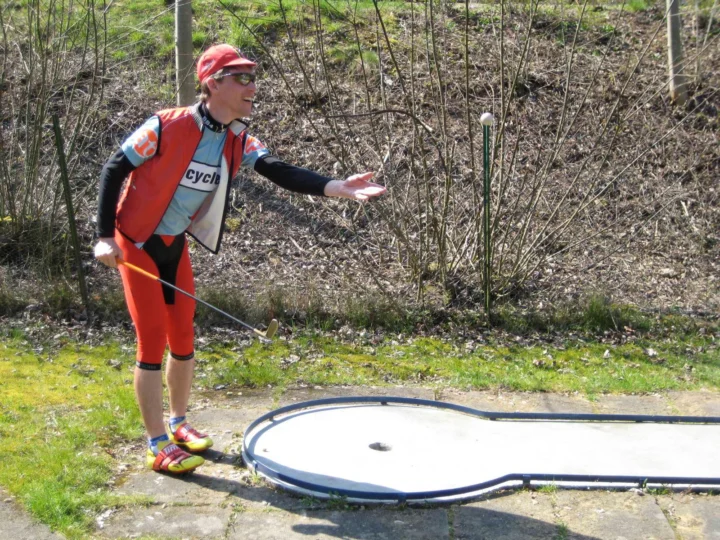 Ein Sportler in orangefarbenem Trikot steht mit Skirollern auf einem Waldweg
