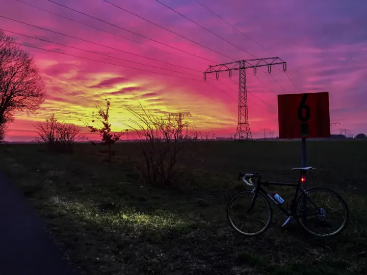 Ein Rennrad steht am Wegrand vor einem rot-violetten Sonnenaufgang