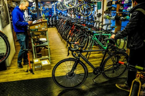 Ein Kunde und ein Verkäufer im Laden, dazwischen die Reihe der ausgestellten Räder