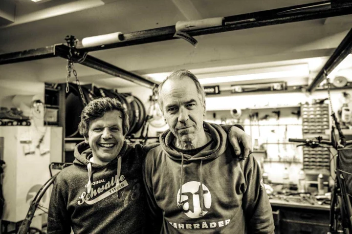 Fabian und Jens Arm in Arm in der Werkstatt, Jens im at-Fahrräder-Pullover