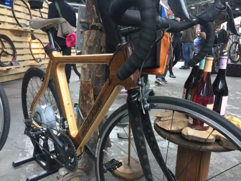 Ein Rennrad mit Rahmen aus Holz zwischen Weinflaschen