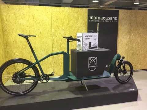 Ein dunkelgrünes Lastenrad mit langer Ladefläche vor einer Sperrholzwand