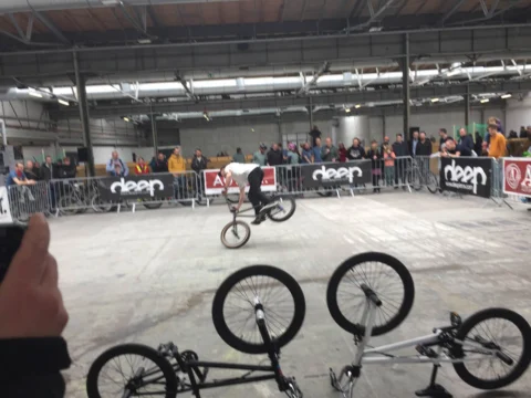 Ein BMX-Fahrer in der Luft über einer Rampe, dahinter Zuschauer hinter Absperrgittern