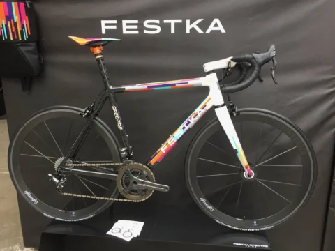 Ein Festka-Rennrad mit bunt gesprenkelter Lackierung vor schwarzer Standwand