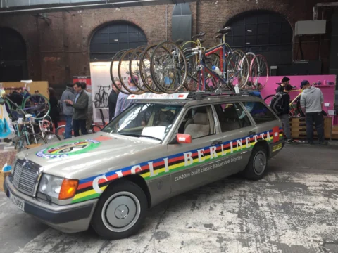 Ein alter Mercedes-Kombi als Teamwagen mit Rennrädern auf dem Dach, beschriftet „Cicli Berlinetta“