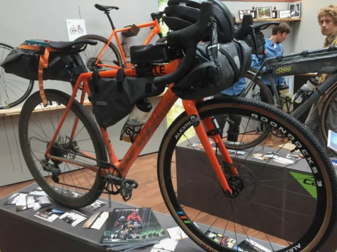 Ein oranges Gravelbike mit Rahmen- und Lenkertaschen auf einem Ausstellungstisch