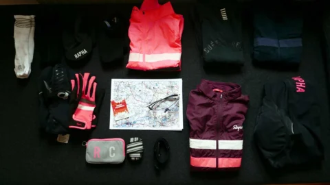Ausrüstung für ein Brevet flach ausgelegt: Jacken, Handschuhe, Karte, Brille und Tasche