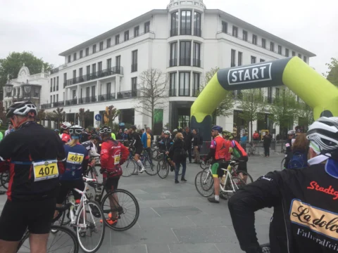 Ein dicht gedrängtes Starterfeld unter einem Startbogen vor einem hellen Hotelgebäude