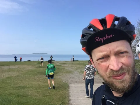 Selfie eines Fahrers mit Helm und Rennmütze, dahinter die Küste und der Zielbereich