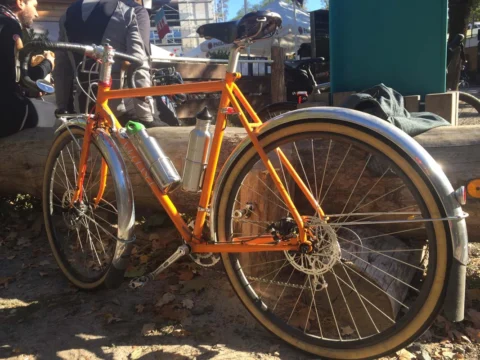 Ein oranger Randonneur mit Schutzblechen und Ledersattel steht im Laub