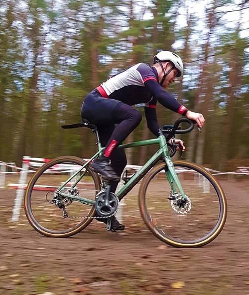 Ein Fahrer auf einem grünen Gravelbike beschleunigt über laubbedeckten Boden