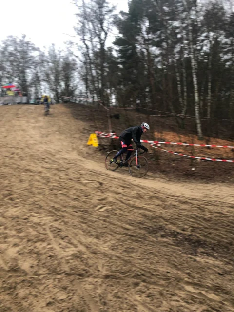 Ein Fahrer quert die weite Sandfläche, dahinter Absperrband und Wald