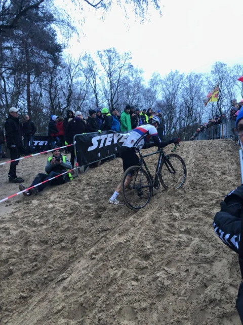 Ein Fahrer schiebt sich durch tiefen Sand, dahinter dicht stehende Zuschauer