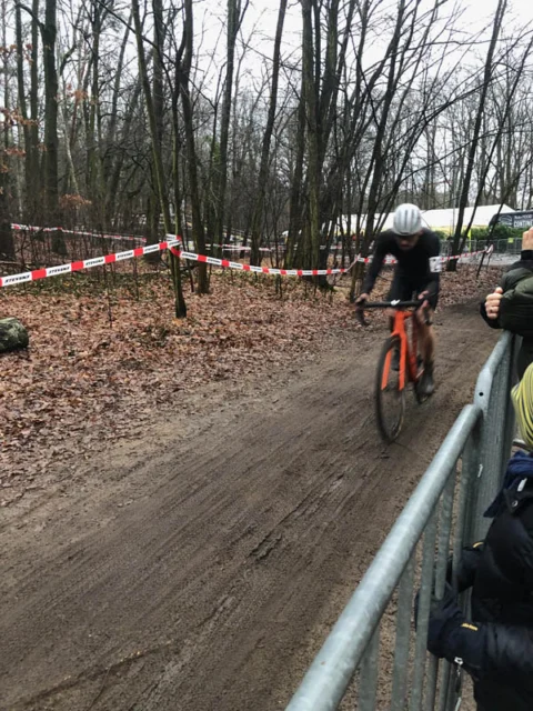Ein Fahrer kämpft sich einen matschigen Anstieg hinauf, rechts Zuschauer am Gitter