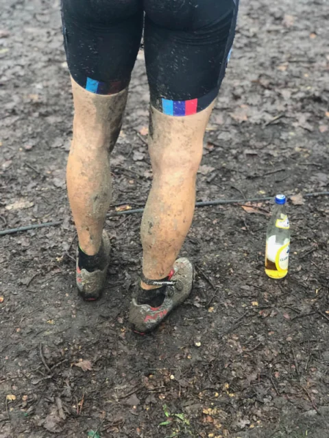 Schlammbespritzte Beine und Schuhe eines Fahrers nach dem Rennen, daneben eine Trinkflasche