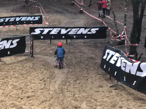 Ein Kind auf einem kleinen Rad fährt durch die Sandpassage zwischen den Banden