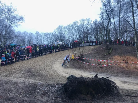 Blick über eine matschige Kurve mit Wurzelstock, dahinter eine dichte Zuschauerreihe