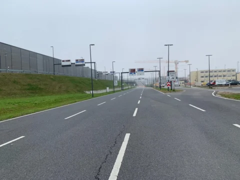 Eine breite, leere Zufahrtsstraße neben einem Erdwall, dahinter Terminalgebäude