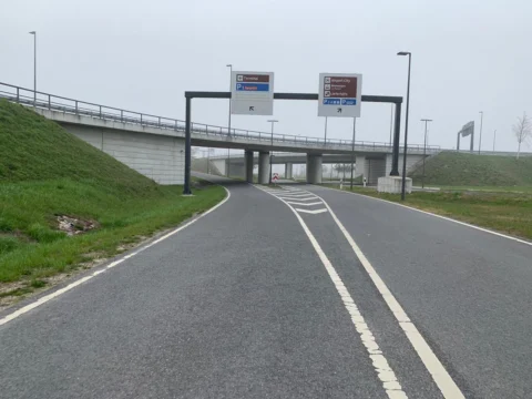 Eine leere Fahrbahn führt unter eine Brücke mit Wegweisern