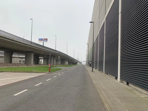 Eine leere Straße entlang einer geriffelten Fassade, links eine Hochstraße