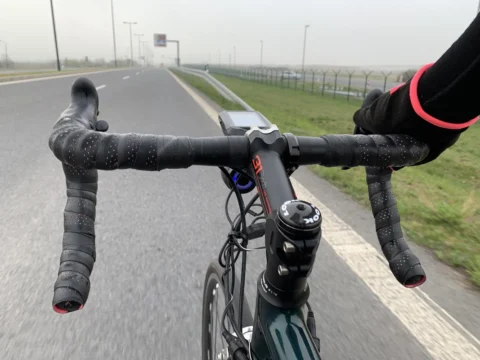 Blick über den Lenker auf einen Radweg neben der Fahrbahn, die Hand am Bremsgriff