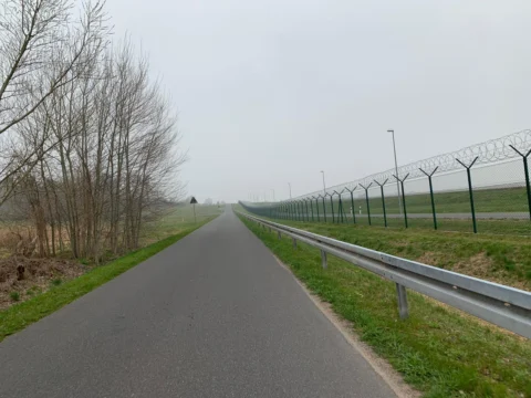 Eine schnurgerade Straße neben dem Zaun des Flughafengeländes im Dunst