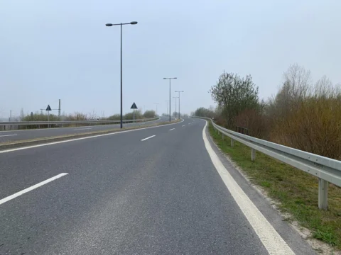 Eine leere Straße führt an einer Leitplanke entlang unter blassem Himmel