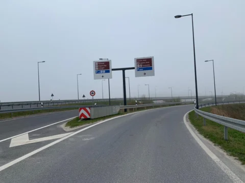 Eine leere Zufahrtsschleife mit Wegweisern und Absperrbake im Nebel